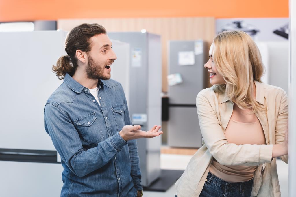 novio sorprendido mirando novia sonriente en la tienda de electrodomésticos
  - Foto, Imagen