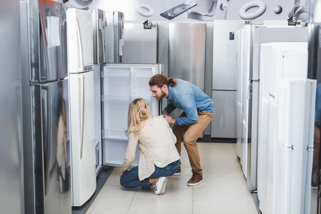 novio y novia hablando cerca de nevera abierta en la tienda de electrodomésticos
  - Foto, Imagen