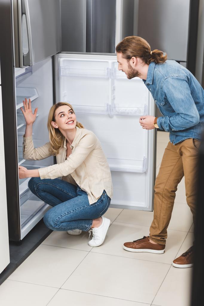 fidanzato parlando con sorridente fidanzata vicino frigorifero in elettrodomestici negozio
  - Foto, immagini