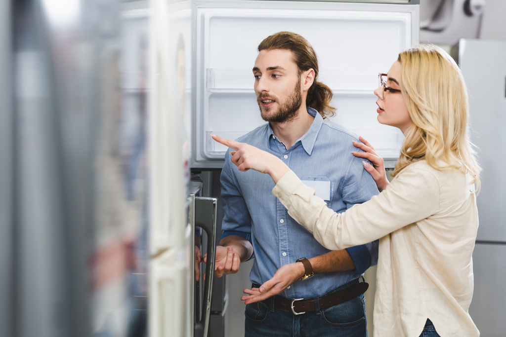 femme parlant avec consultant et pointant du doigt au réfrigérateur dans le magasin d'appareils ménagers
  - Photo, image