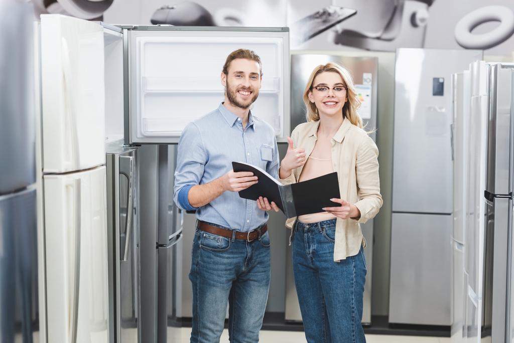 Lächelnder Berater hält Ordner in der Hand und Frau zeigt wie im Haushaltsgerätegeschäft  - Foto, Bild