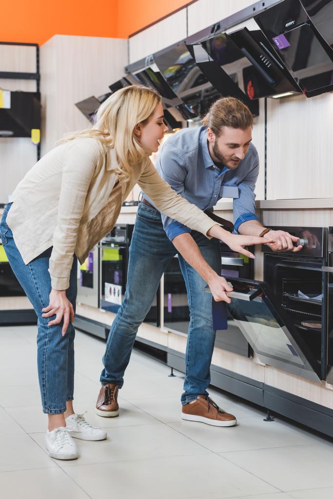 consultant use oven and smiling woman pointing with hand in home appliance store  - Photo, Image