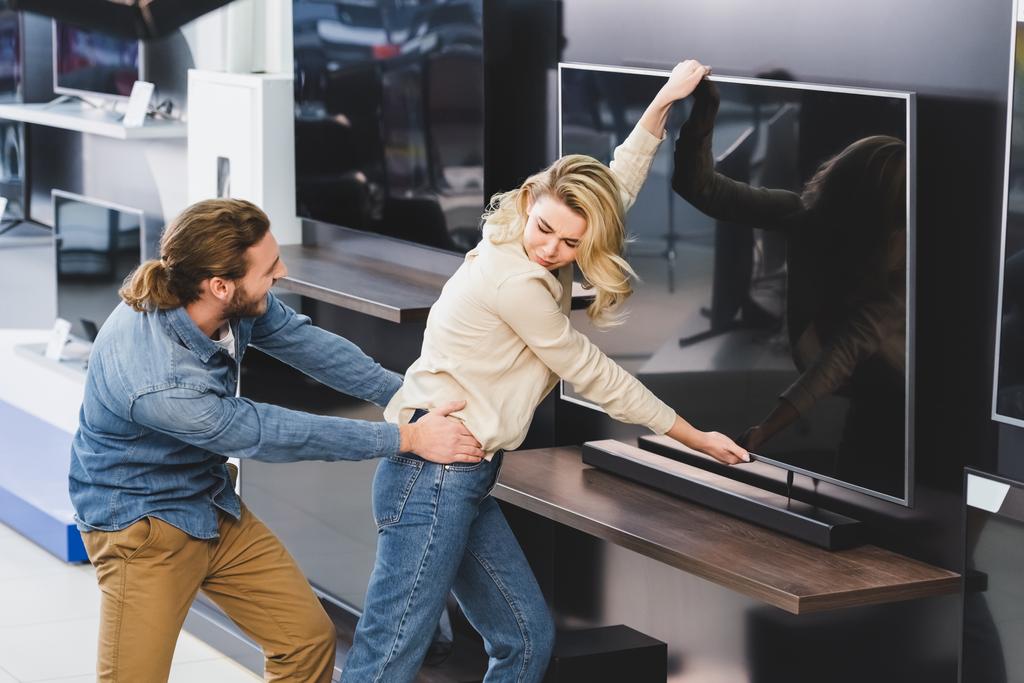 сердитий хлопець тягне дівчину з телевізором в магазині побутової техніки
  - Фото, зображення