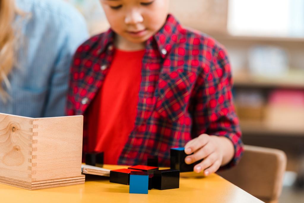 Concentration sélective de l'enfant jouant des blocs de construction à côté du professeur à l'école montessori
 - Photo, image