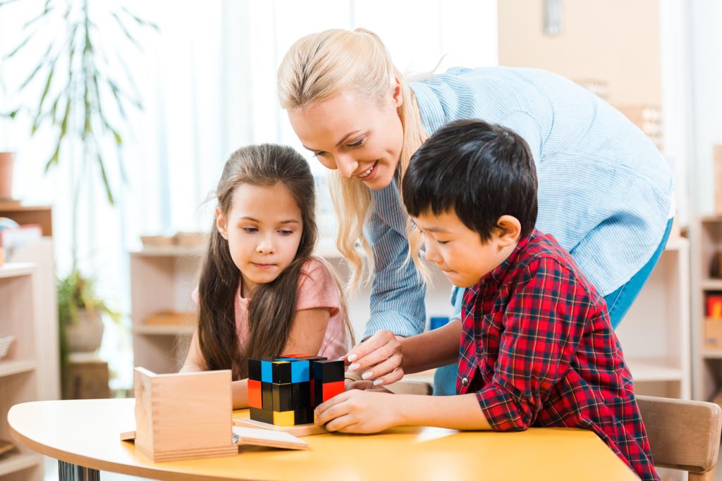 Professora sorrindo jogando blocos de construção com crianças durante a aula de montessori
  - Foto, Imagem