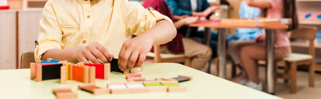 Panoramiczne ujęcie dziecka grającego w edukacyjną grę z dziećmi w tle w szkole montessori, widok przycięty - Zdjęcie, obraz