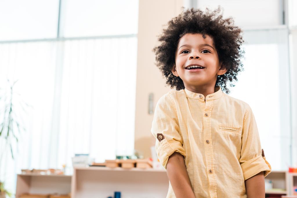 Visão de baixo ângulo da criança afro-americana sorrindo enquanto olha para longe
 - Foto, Imagem