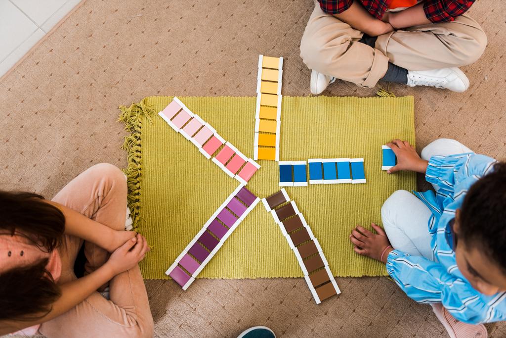 Вид сверху на детей, играющих в красочную игру на полу в школе Монтессори
 - Фото, изображение