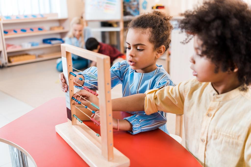 Concentration sélective des enfants afro-américains jouant avec des partitions avec le professeur et l'enfant en arrière-plan à l'école montessori
 - Photo, image