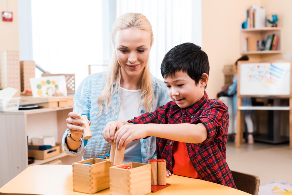 asiatisches Kind spielt Brettspiel von lächelndem Lehrer am Schreibtisch in der Montessori-Schule - Foto, Bild
