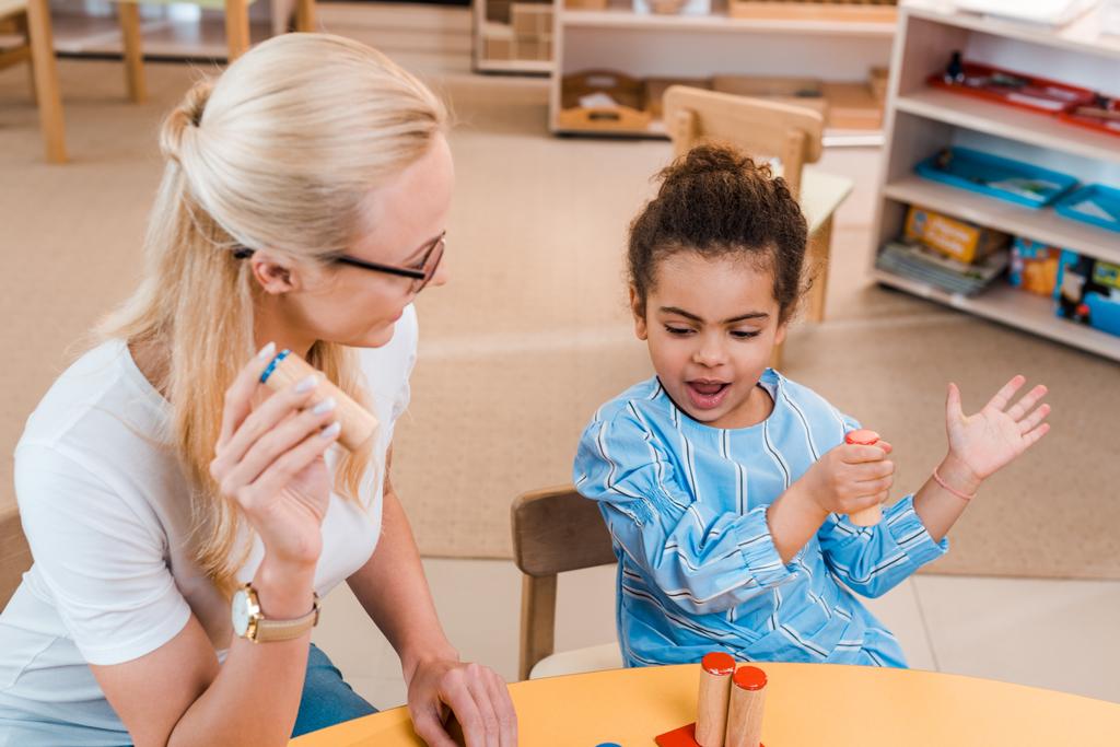 Profesor jugando juego educativo con el niño en el escritorio en la escuela montessori
 - Foto, Imagen