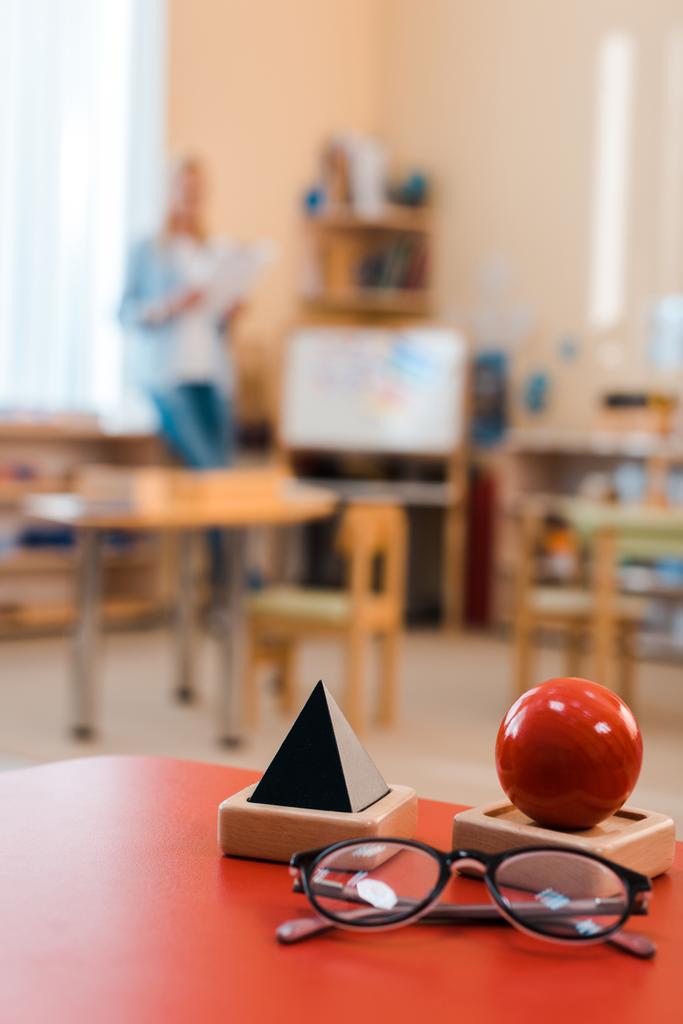 Вибірковий фокус освітньої гри та окуляри на столі з вчителем на фоні школи Монтессорі
 - Фото, зображення