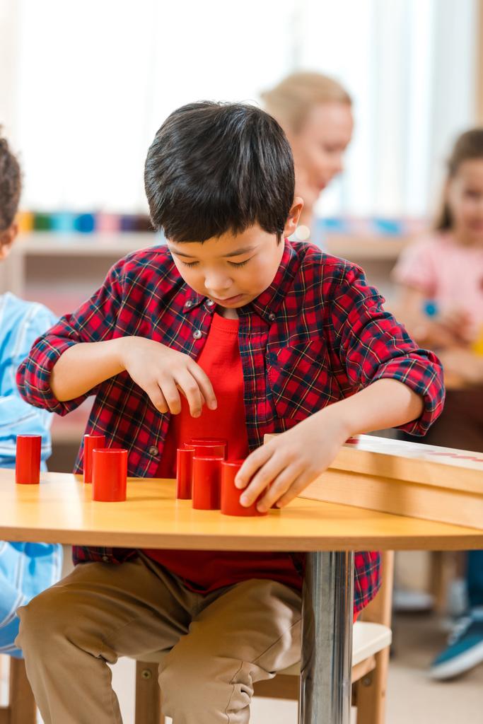 Selektivní zaměření asijské dítě skládací vzdělávací hra s učitelem a dětmi na pozadí v Montessori třídě - Fotografie, Obrázek