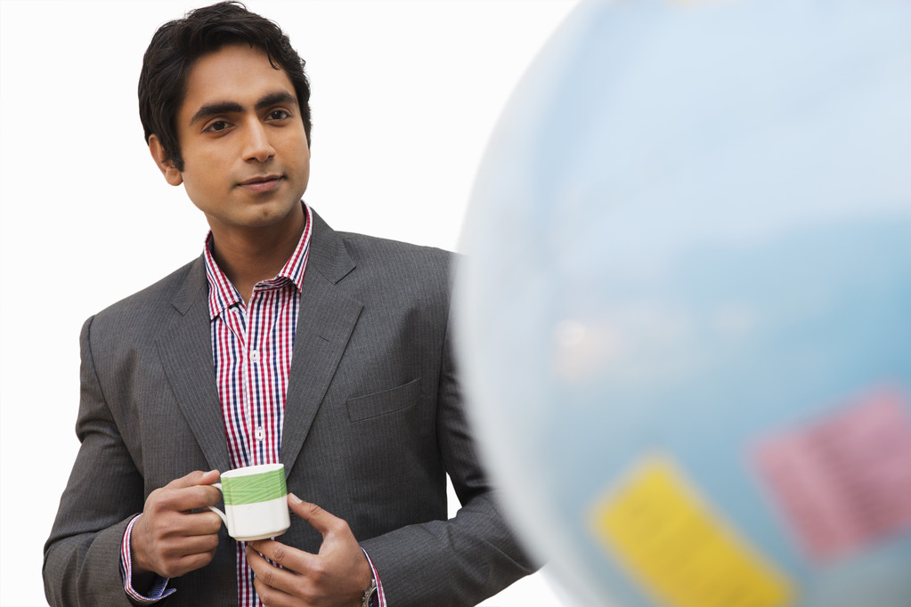 Бизнесмен держит чашку чая и смотрит на глобус
 - Фото, изображение