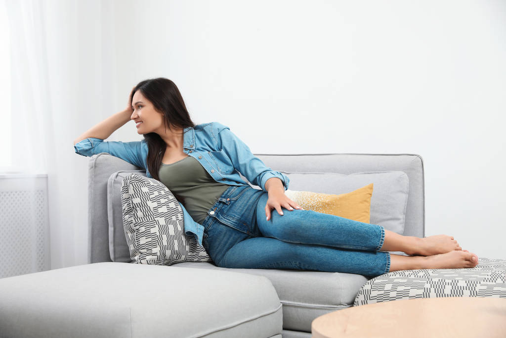 Νεαρή γυναίκα χαλαρώνοντας στον καναπέ στο σπίτι - Φωτογραφία, εικόνα