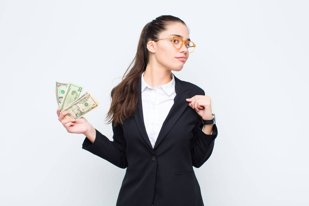 junge Geschäftsfrau sieht arrogant, erfolgreich, positiv und stolz aus und zeigt auf sich selbst mit Banknoten mit Scheinen - Foto, Bild