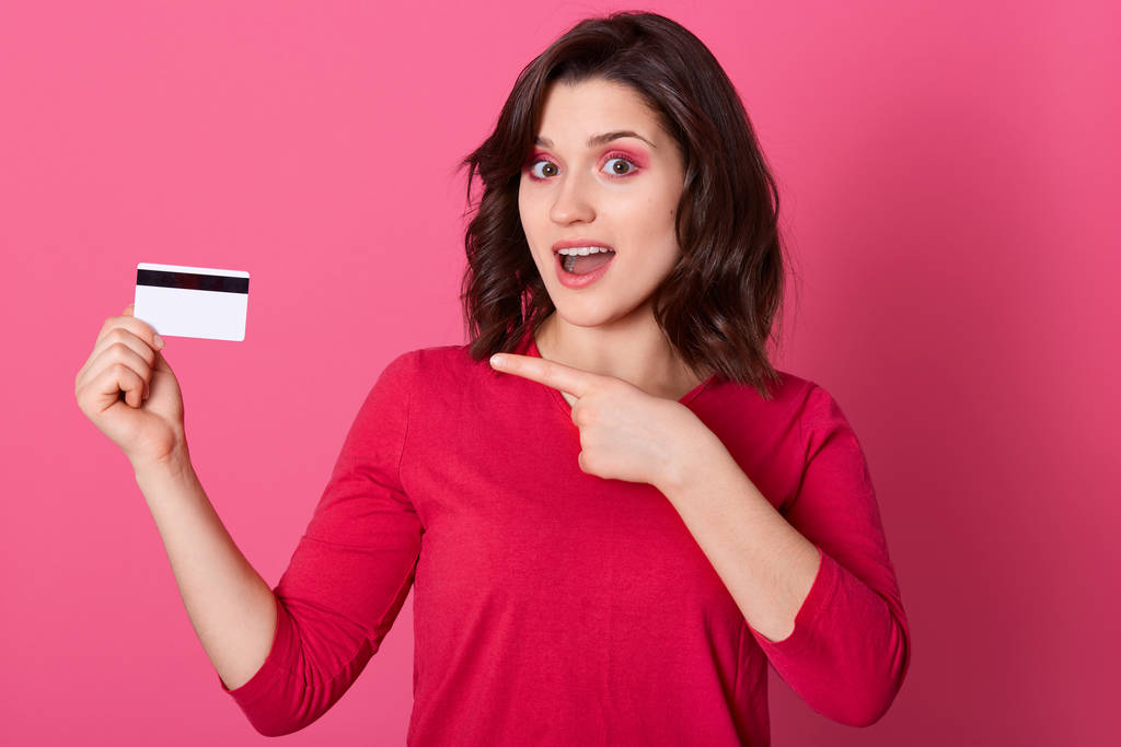 Bild von emotional gut aussehenden hübschen Frauen, die mit dem Zeigefinger auf Kreditkarte zeigen, überraschten Gesichtsausdruck haben, den Mund öffnen, online einkaufen. Frauen und Kaufkonzept. - Foto, Bild