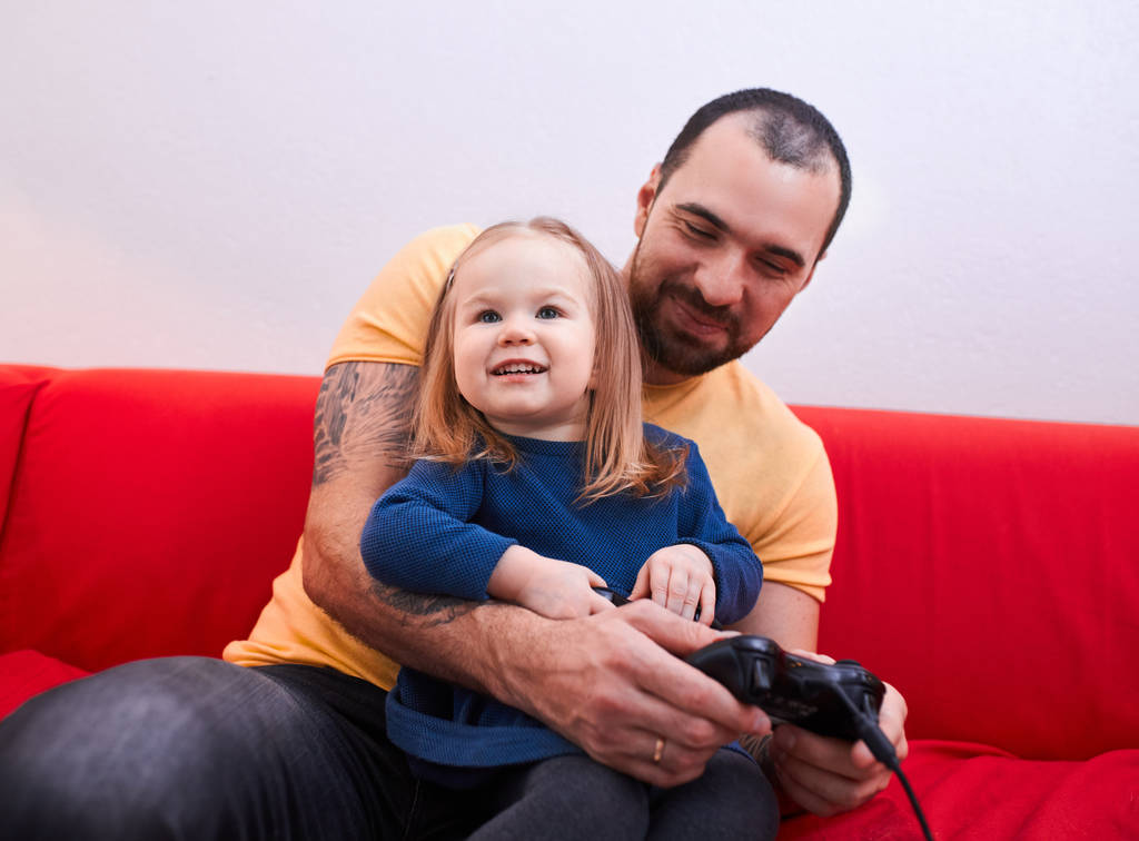 χαριτωμένο κορίτσι κάθονται με τον πατέρα, ενώ παίζει βιντεοπαιχνίδια - Φωτογραφία, εικόνα