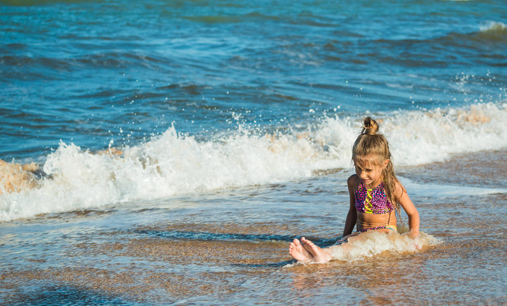 Deniz kıyısında oturan küçük pozitif kız - Fotoğraf, Görsel