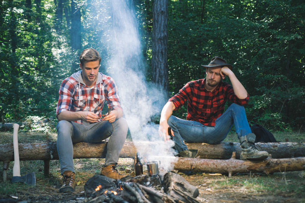Družina dva mužští přátelé si užívají odpočinku v lese. Šťastní mladí lidé táboří v lese. Přátelé sedí na lesním pikniku. Skupina dvou samců Backpackers relaxaci v blízkosti táboráku. - Fotografie, Obrázek