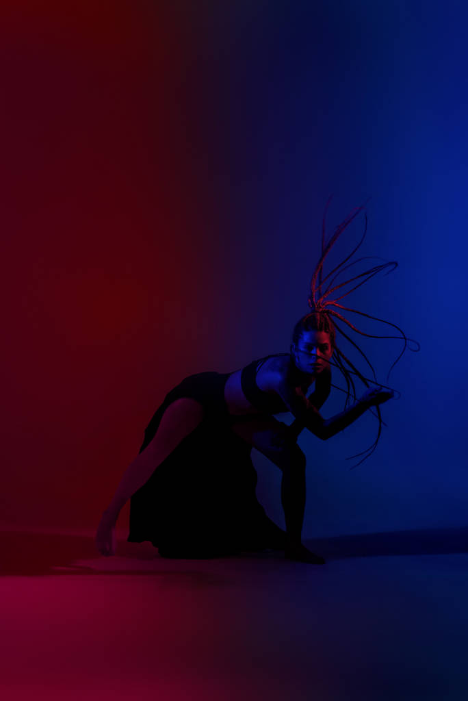Черная одетая и заплетенная волосы женщина танцует на синем и красном
 - Фото, изображение