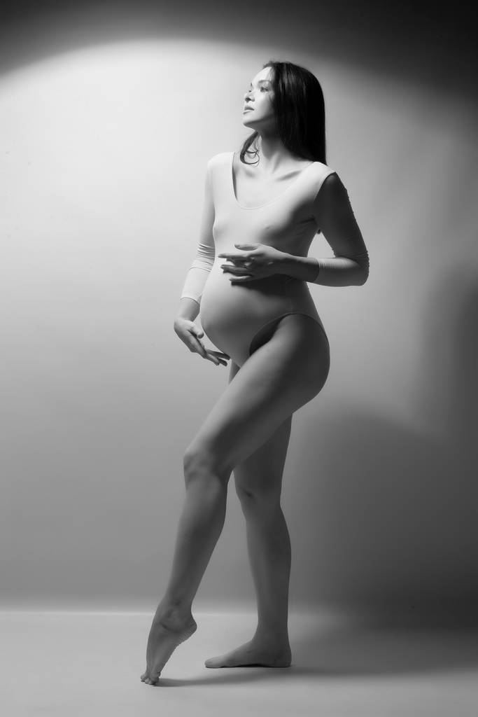 Femme enceinte en body blanc sur fond gris
. - Photo, image