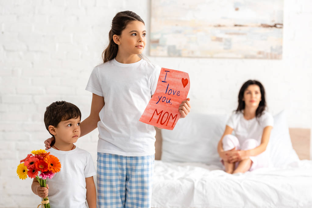cute brother and sister holding i love you mom card and flowers, while mother sitting in bed - Photo, Image
