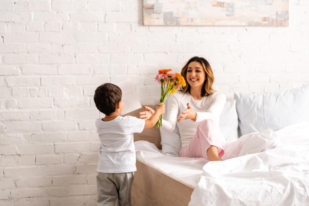 visão traseira do menino apresentando flores e mães cartão de dia para a mãe feliz
 - Foto, Imagem