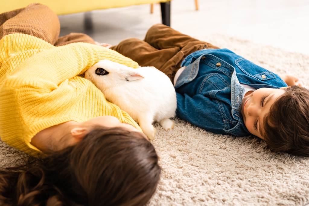 adorable hermano y hermana acostado en el suelo cerca blanco divertido conejo
 - Foto, Imagen