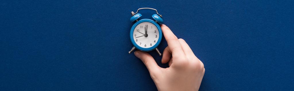 vista recortada de la mujer sosteniendo pequeño reloj despertador sobre fondo azul, tiro panorámico
 - Foto, Imagen