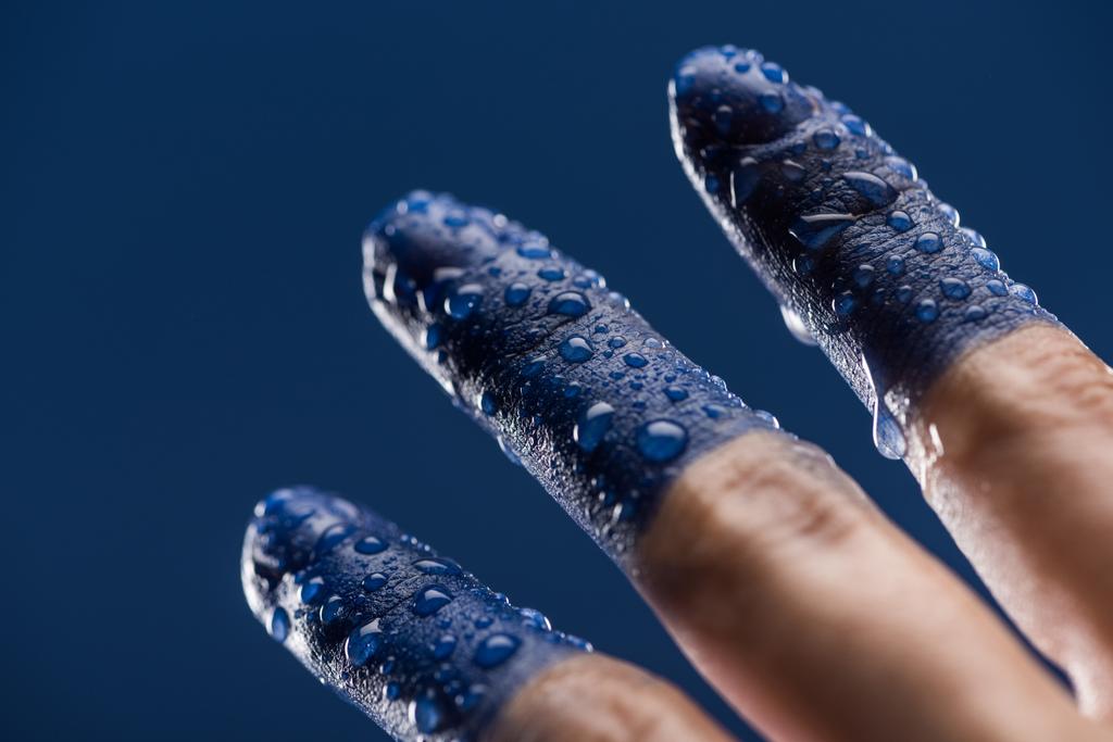 στενή άποψη του θηλυκού χεριού με βρεγμένα βαμμένα δάχτυλα απομονωμένα στο μπλε - Φωτογραφία, εικόνα