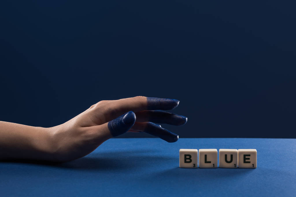 青い文字が青い文字で区切られた立方体の近くに描かれた指で女性の手のクロップドビュー - 写真・画像
