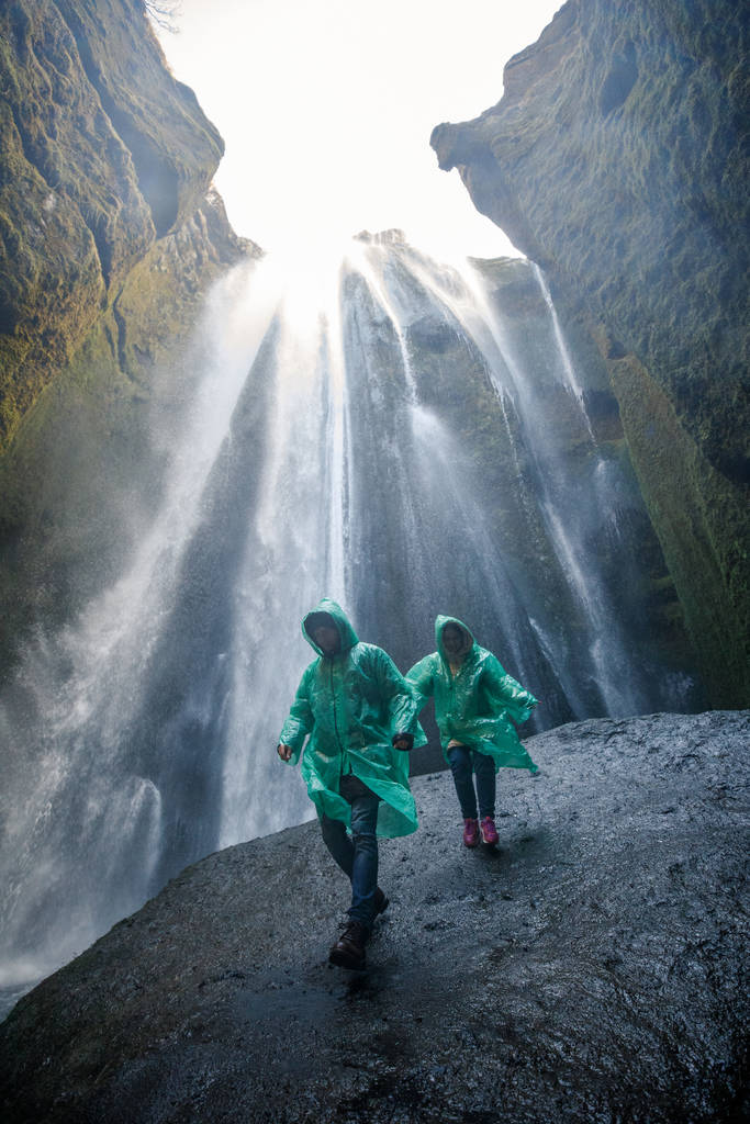 pareja en impermeables verdes caminando cerca de la cascada en las montañas de hielo
 - Foto, imagen