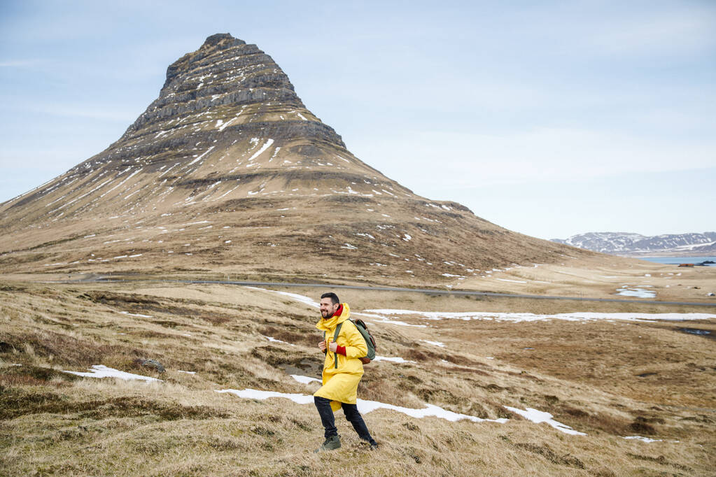 man in gele jas wandelen op vallei in IJsland bergen achtergrond - Foto, afbeelding