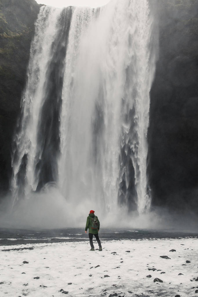 アイスランドの山の上の滝の近くに立つ若いハンサムな男背景 - 写真・画像