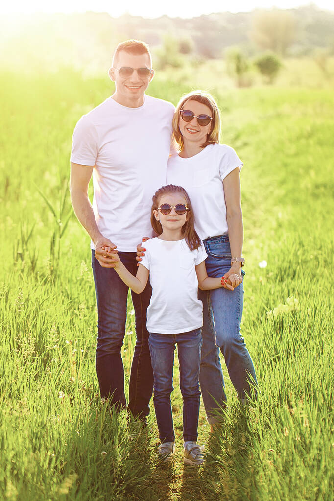 Beyaz tişörtlü, güneş gözlüklü ve kot pantolonlu mutlu bir aile fotoğrafı. Yaz - Fotoğraf, Görsel