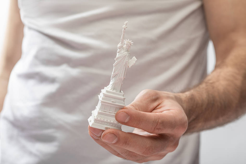 καλλιεργημένη άποψη του άνδρα που κρατά το άγαλμα της ελευθερίας απομονωμένο σε λευκό  - Φωτογραφία, εικόνα