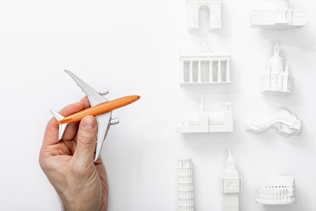 cropped view of man holding toy plane near statuettes from different countries of europe isolated on white  - Photo, Image