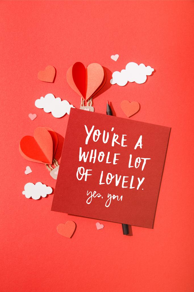 top view of paper heart shaped air balloons in clouds near card with you're a whole lot of lovely yes, you lettering on red background - Photo, Image