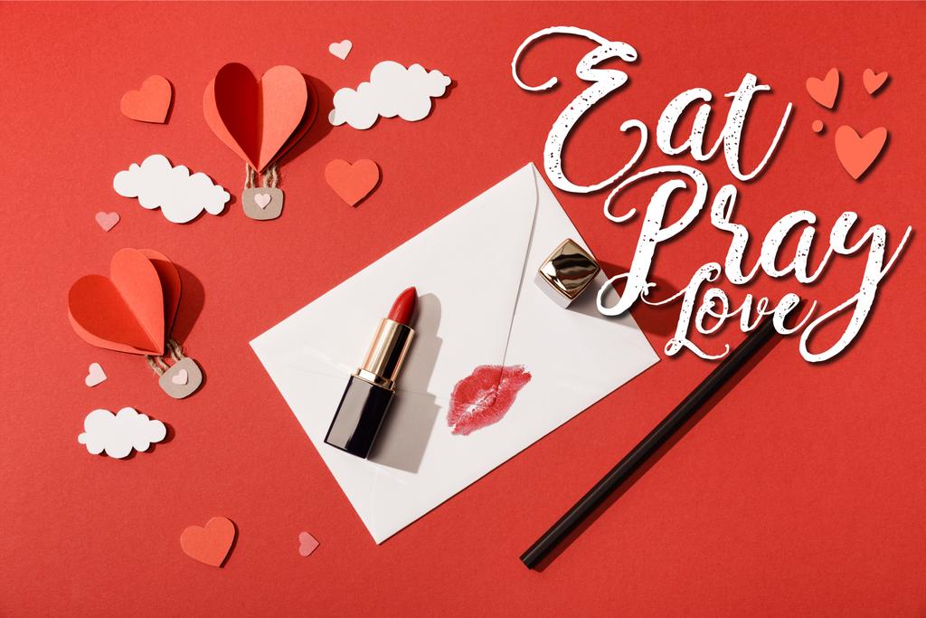 vue du dessus des nuages de papier et des ballons à air en forme de coeur, rouge à lèvres et crayon près de l'enveloppe avec impression sur les lèvres et manger prier l'amour lettrage sur fond rouge
 - Photo, image