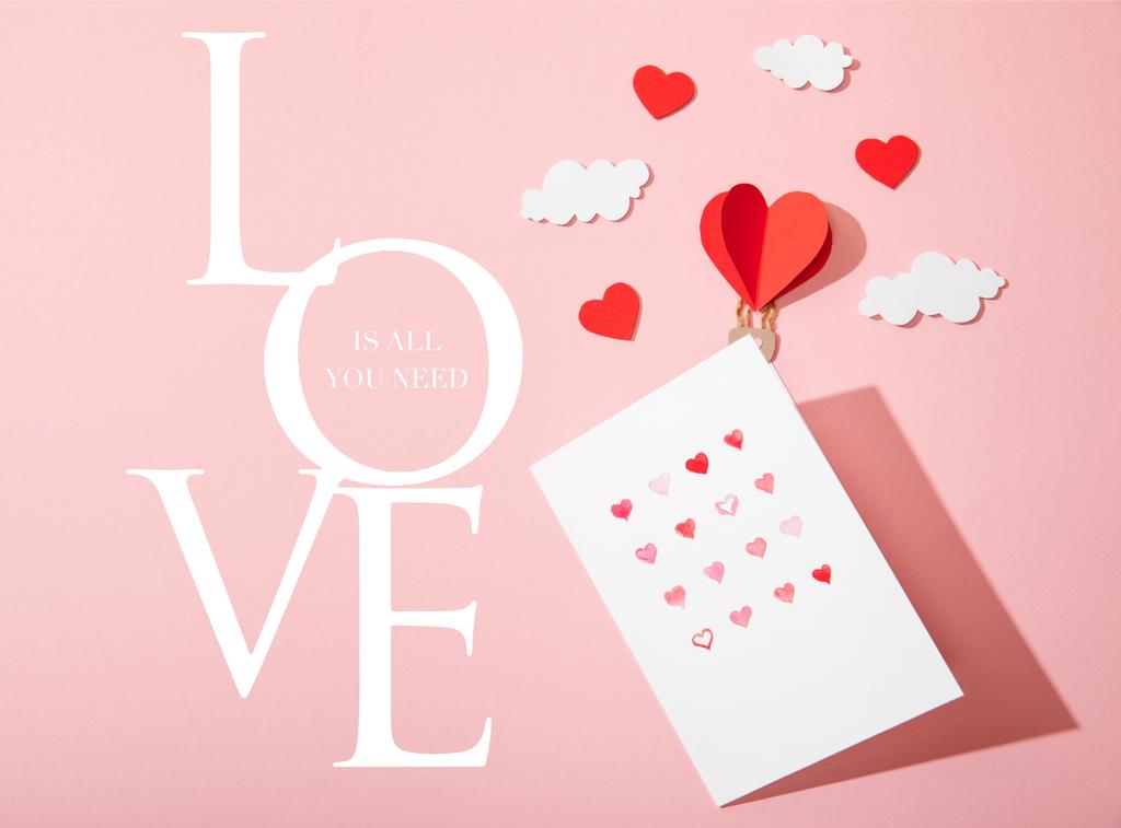 Kağıt kalpli tebrik kartının en üst görüntüsü bulutlarda hava balonu ve pembe harflerle yazılmış aşk. - Fotoğraf, Görsel