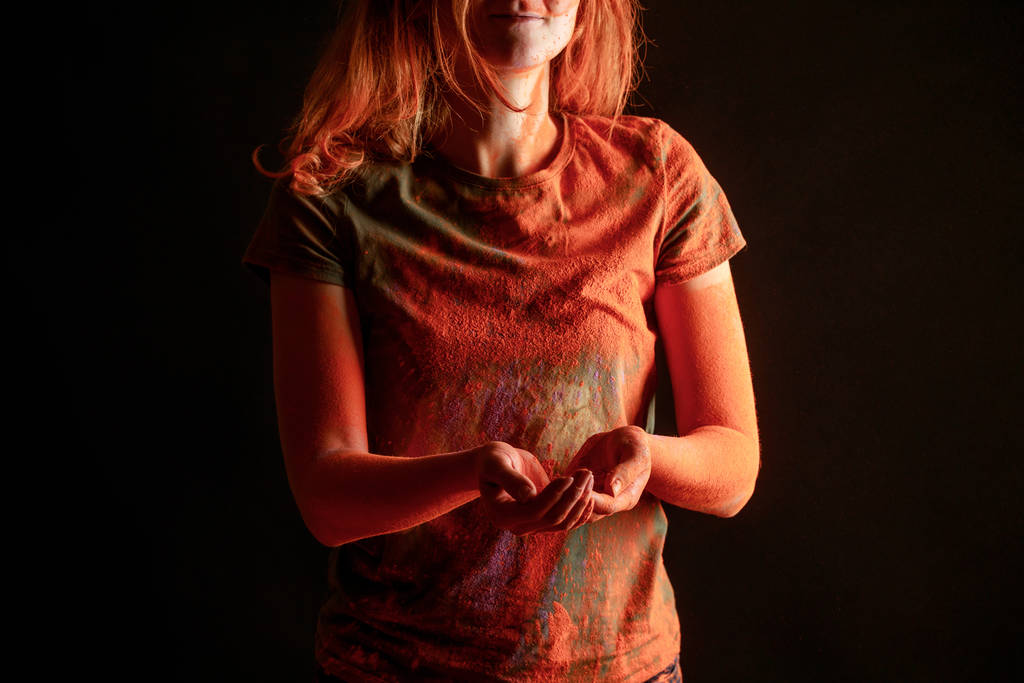 vista recortada de la mujer con polvo de pintura holi de color naranja aislado en negro
 - Foto, imagen