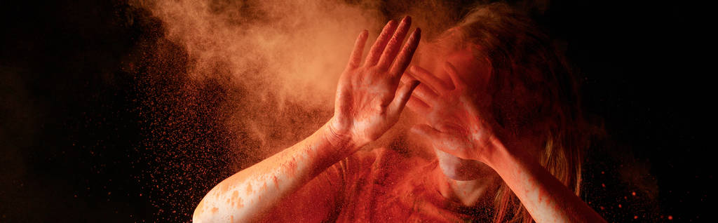 mulher cobrindo rosto de laranja colorido holi pintura nuvem no fundo preto, tiro panorâmico
 - Foto, Imagem