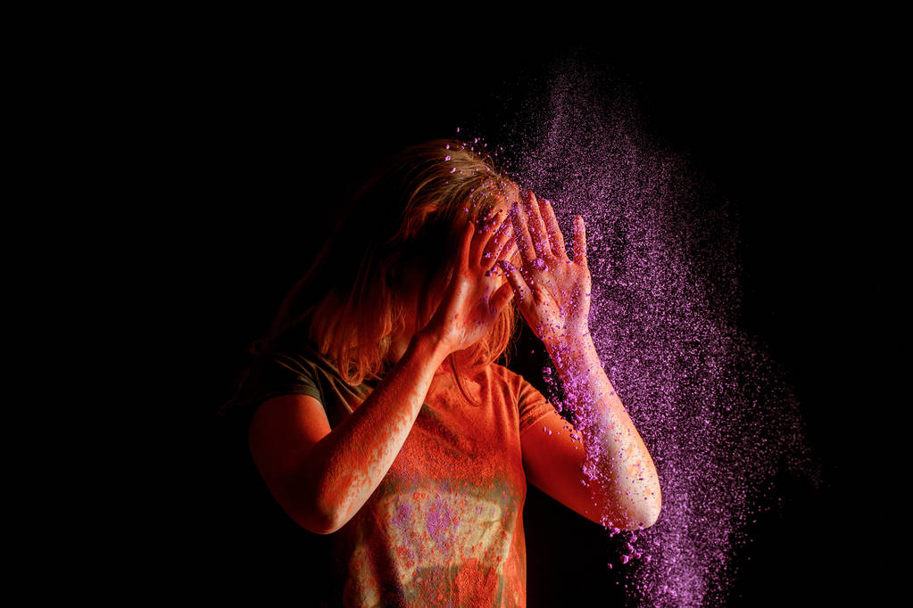 woman covering face from violet colorful holi paint cloud on black background - Photo, Image