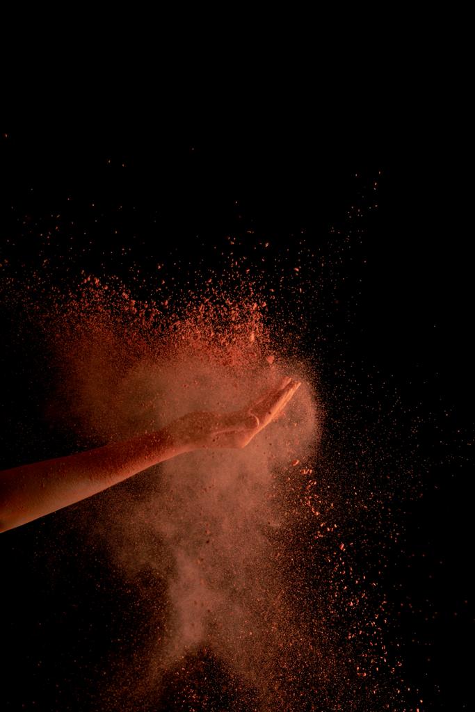 vista recortada de la mano femenina con pintura holi de color naranja estallido sobre fondo negro
 - Foto, Imagen