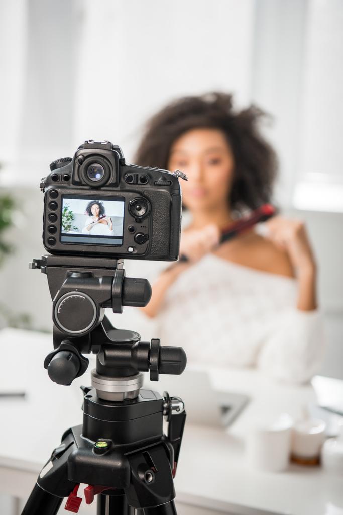 Ekranda saç düzleştirici kullanan kıvırcık Afrikalı Amerikalı etkileyiciyle dijital kameranın seçici odağı  - Fotoğraf, Görsel
