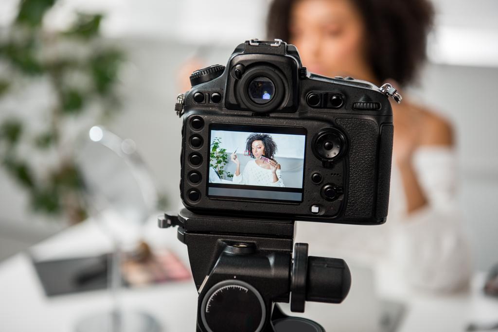 selectieve focus van digitale camera met Afrikaans Amerikaans meisje met palet met lipgloss en cosmetische borstel op display  - Foto, afbeelding