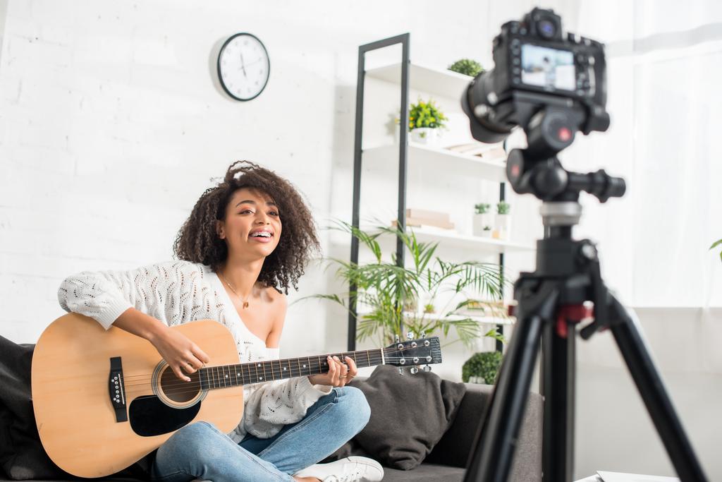 enfoque selectivo de la chica afroamericana feliz en frenos tocando la guitarra acústica cerca de la cámara digital
  - Foto, Imagen