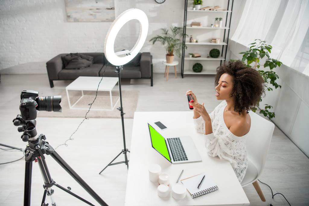 Afrikanisch-amerikanischer Influencer mit Haarglätter in der Nähe von Digitalkamera und Laptop mit grünem Bildschirm  - Foto, Bild