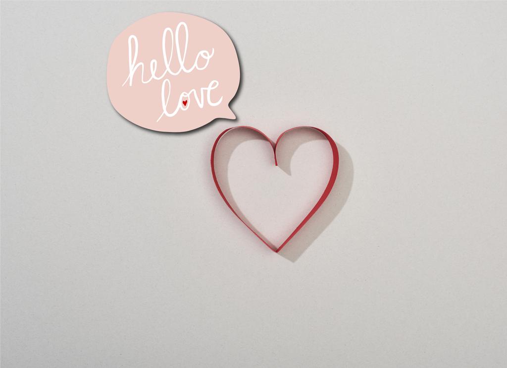 Bovenaanzicht van rood papieren hart op grijze achtergrond met hello love belettering in spraakbel - Foto, afbeelding